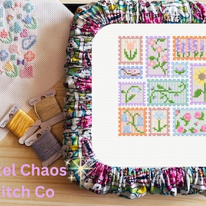 May include: A cross-stitch project featuring floral designs, including a tulip, roses, and a sunflower. The project is set in a white frame with a colorful fabric border. Several spools of DMC thread in yellow, beige, and gray are visible.