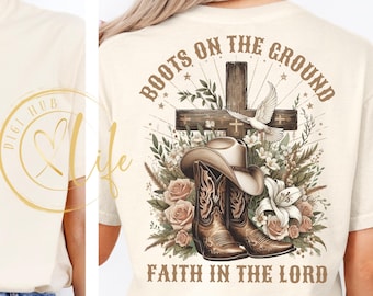 May include: Cream-colored t-shirt featuring a graphic design on the back. The design includes a cowboy hat, boots, a cross, and the text "BOOTS ON THE GROUND FAITH IN THE LORD". The design is surrounded by flowers and a dove.