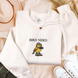 Könnte beinhalten: Ein Set aus drei Keramikbechern mit gesprenkelter, matter Oberfläche. Die Becher sind in den Farbtönen Creme, Hellgrau und Dunkelgrau gehalten. Jeder Becher hat ein schlichtes, minimalistisches Design und einen abgerundeten Griff.