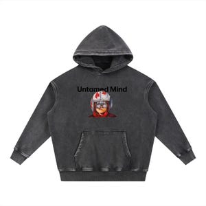 May include: A dark grey hoodie with a front pocket and a hood. The hoodie displays the text "Untamed Mind" above an illustration of a person wearing a pilot helmet and goggles. The hoodie is made of a soft, comfortable material.