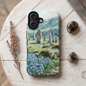 Op de afbeelding: Een smartphonehoesje met een gedetailleerd landschapsschilderij van staande stenen in een grasveld met blauwe wilde bloemen op de voorgrond. Het kunstwerk toont een glooiende groene heuvel onder een heldere lucht, met een uitsparing voor de camera.