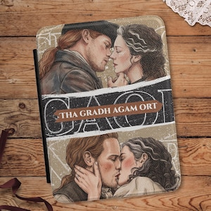 May include: A rectangular tablet case featuring two illustrated scenes of a couple. The top shows them facing each other, while the bottom shows them kissing. A central black banner displays the text "THA GRADH AGAM ORT" in white letters.