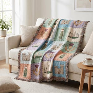 Puede incluir: Manta tejida con un diseño de patchwork con flores de cardo escocés, castillos y tarros de hierbas en colores pastel. La manta está sobre un sofá beige, con bordes con flecos.