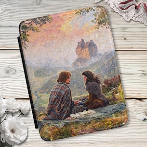 Puede incluir: Una funda rectangular para lector electrónico con una pintura de paisaje impresa de dos personas sentadas en una colina cubierta de hierba. La escena incluye un castillo de piedra a lo lejos bajo un cielo suave y brumoso, con ropa texturizada.