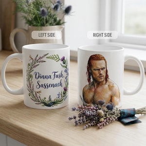 May include: White ceramic mug with a handle. The left side features text within a floral wreath, while the right side displays a portrait of a man with red hair. A small bouquet of lavender and thistles rests nearby.