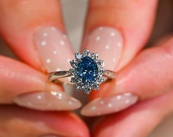 Könnte beinhalten: Ein silberner Ring mit einem ovalen, blauen Edelstein in der Mitte, umgeben von kleineren, klaren Steinen. Der Ring wird präsentiert, um sein Design und seinen Glanz hervorzuheben. Der Ring ist ein Schmuckstück.