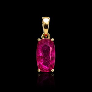 May include: A rectangular cushion-cut vibrant pinkish-red gemstone pendant set in a polished yellow gold four-prong setting with a matching gold bail at the top, showcasing a faceted surface that reflects light against a solid black background.