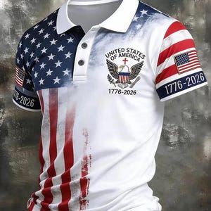 Puede incluir: Un polo blanco con un diseño basado en la bandera estadounidense. La camisa tiene cuello y mangas blancos con las estrellas y rayas de la bandera. El texto "UNITED STATES OF AMERICA 1776-2026" está impreso en la parte delantera.
