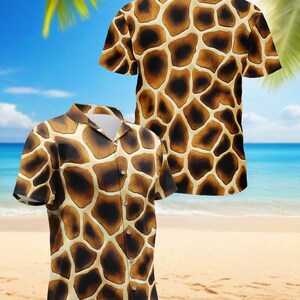 Op de afbeelding: Twee shirts met korte mouwen en knopen met een giraffenpatroon. De shirts hebben een bruin en beige patroon, met een kraag en knopen. De achtergrond toont een strandscène met palmbomen, zand en blauw water.