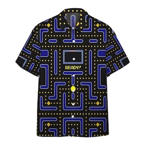 Pode incluir: Camisa preta com botões com um design de videogame Pac-Man. A camisa apresenta um padrão de labirinto em azul e amarelo sobre um fundo preto. A palavra "READY!" é impressa na frente.