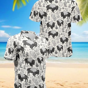 May include: White button-up shirt with a black and gray bison and cactus pattern. The short-sleeved shirt has a classic collar and is made of a lightweight fabric. The design features detailed illustrations of bison and cacti.