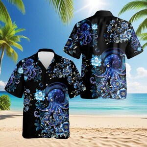 Puede incluir: Camisa negra de manga corta con un diseño de pulpo azul y floral. El diseño incluye una escena de playa tropical. El pulpo está rodeado de flores y follaje azules, creando un contraste llamativo.