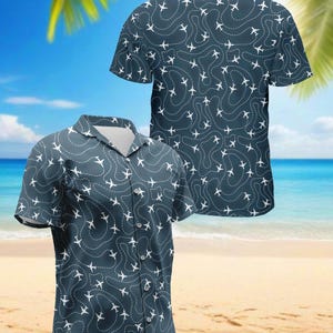 May include: A short-sleeved button-down shirt with a dark teal background and a repeating pattern of white airplanes and dotted flight paths. The shirt has a classic collar and a relaxed fit, perfect for casual wear.