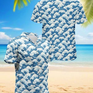 May include: Two short-sleeved button-down shirts with a blue and white wave pattern. The shirts have a classic collar and are displayed on a beach background with palm trees and the ocean. The wave design is repeated across the fabric.