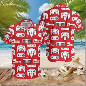 May include: Red short-sleeved button-down shirt featuring a pattern of white and gray video game controllers and consoles. The shirt has a classic collar and is displayed on a sandy beach setting.