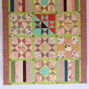 May include: A patchwork quilt with a variety of floral and geometric patterns in shades of pink, green, brown, and yellow. The quilt is made up of 9 squares, each with a different design. The quilt is hanging on a white wall.