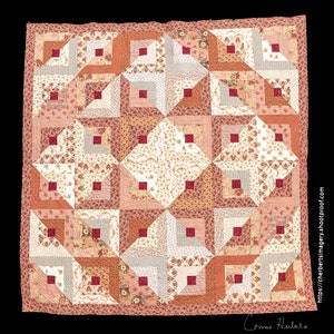 May include: A quilt made of various shades of pink and red fabric with a floral pattern. The quilt is made up of squares and triangles, and the squares have a smaller square in the center. The quilt is signed "Corinne Herlato" in the bottom right corner.