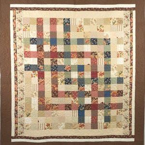 May include: A patchwork quilt with a grid pattern of squares and rectangles in various colors and floral patterns. The quilt has a brown border and a cream-colored inner border with floral designs. The quilt measures approximately 70 inches by 70 inches.