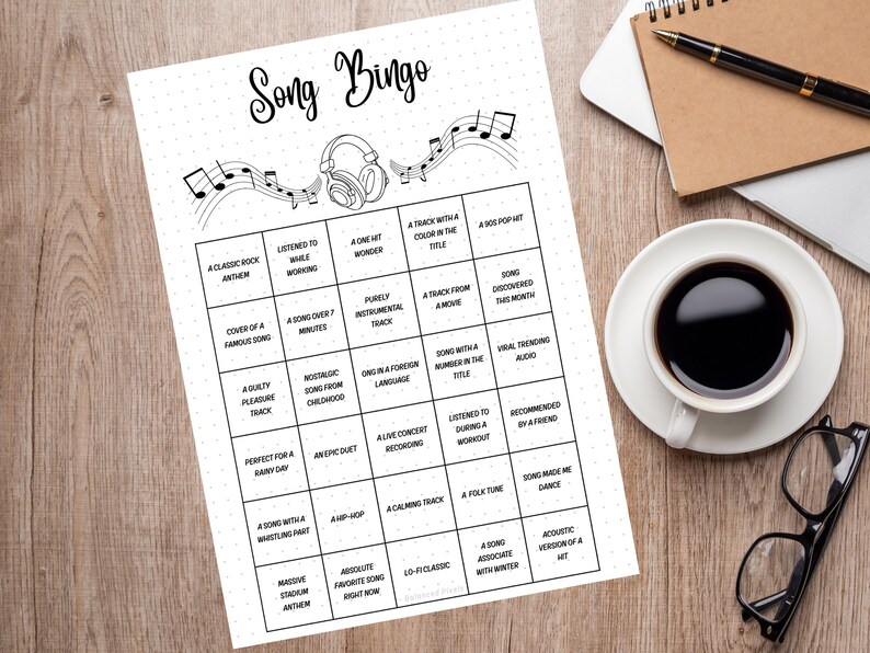 May include: A black and white "Song Bingo" game sheet with music notes and a headphone graphic. The bingo card has various music-related prompts. The sheet is on a wooden surface, next to a coffee cup, glasses, a pen, and a notebook.