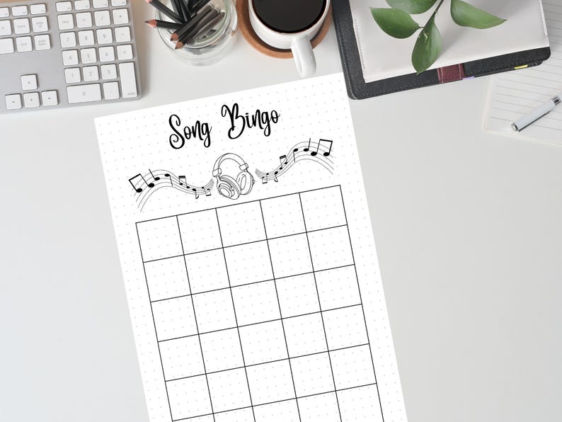 May include: A black and white Song Bingo game sheet with a grid of squares. The title "Song Bingo" is written in cursive above a musical staff with notes and headphones. The sheet is on a white surface.
