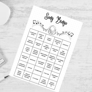 May include: A black and white "Song Bingo" game sheet with musical notes and a headphone graphic. The game sheet has a grid of squares with music-related prompts. A white keyboard, mouse, and pen are in the background.
