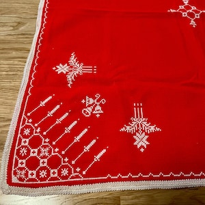 Può includere: Una tovaglia rettangolare rossa con motivi ricamati a punto croce bianco. Il design include forme geometriche, motivi floreali e accenti lineari. I bordi sono rifiniti con una decorativa bordura all'uncinetto di colore bianco.