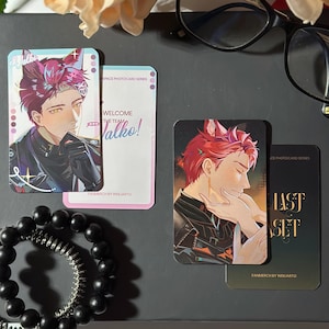 May include: Two rectangular trading cards featuring anime-style illustrations of a character with red hair and animal ears. One card shows the character with the text Valko, while the other shows the character with the text LAST SET. A black beaded bracelet and black-rimmed glasses are also present.
