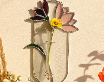 May include: A wall-mounted stained glass flower vase featuring a vertical oval frame with a clear glass test tube holder. The design includes decorative glass petals in shades of dark purple and light pink, with a single yellow flower.