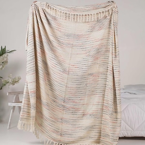 May include: Cream-coloured throw blanket with a stitched pattern of red and navy blue dots. The blanket has a fringed edge and is draped over a bed. This decorative blanket is perfect for adding a touch of warmth and style to any room.
