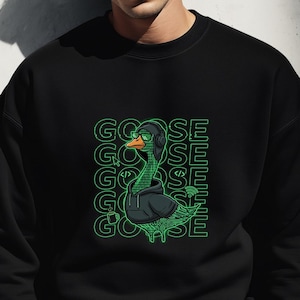 Puede incluir: Sudadera negra con un gráfico verde de un ganso con capucha y gafas de sol. La palabra "GOOSE" está apilada verticalmente en verde. Llevada por una persona.
