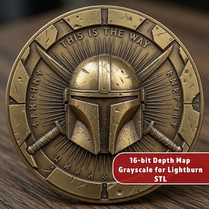 May include: A bronze-colored coin featuring a Mandalorian helmet design. The coin has the phrase "THIS IS THE WAY" inscribed at the top, with additional text and symbols around the edges. The coin also has the text "16-bit Depth Map Grayscale for Lightburn STL".