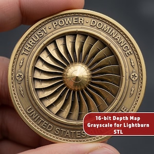 May include: A circular brass-toned metal coin featuring a detailed relief of a jet engine turbine in the center. The outer rim is inscribed with the text THRUST, POWER, DOMINANCE, and UNITED STATES, along with star and lightning bolt symbols.
