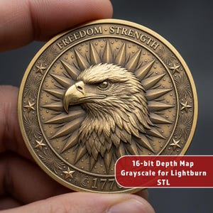 May include: A circular gold-toned coin featuring a relief of an eagle head in the center, surrounded by a sunburst pattern and stars. The text FREEDOM STRENGTH and 1776 are embossed on the rim. A red label reads 16-bit Depth Map Grayscale for Lightburn STL.