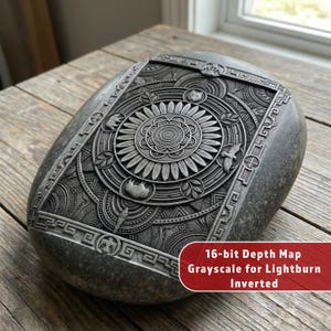 May include: A gray, oval-shaped stone with a detailed, engraved design. The design features a central floral motif surrounded by geometric patterns, birds, and animal figures. The text "16-bit Depth Map Grayscale for Lightburn Inverted" is visible.