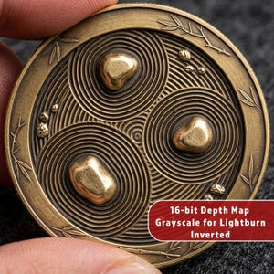 May include: A bronze-colored coin with a zen garden design. The coin features three raised, gold-colored stones within concentric circles. The coin's edge has a decorative leaf pattern. Text on the coin reads: "16-bit Depth Map Grayscale for Lightburn Inverted."