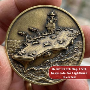 May include: A bronze-colored coin featuring a detailed depiction of an aircraft carrier at sea, with numerous fighter jets on the deck. The coin's design includes the ship's superstructure and the surrounding waves. Text on the coin reads: "16-bit Depth Map + STL Grayscale for Lightburn Inverted."