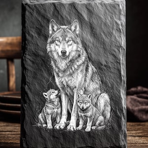 May include: A rectangular black slate featuring a detailed engraving of a wolf and two pups. The adult wolf is centered, with the pups flanking it. The text "LASER READY PNG" is at the top. The image is set against a dark background.
