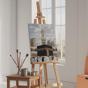 May include: A paint-by-numbers canvas depicting the Kaaba in Mecca, displayed on a wooden easel. The artwork features the black cube-shaped structure, surrounded by a crowd of people. Paintbrushes and containers sit on a small wooden table.
