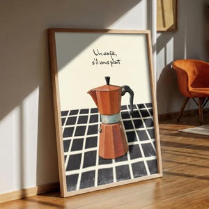 May include: A framed art print depicting a copper-coloured stovetop espresso maker. The print includes the French phrase "Un café, s'il vous plaît" in black script. The background features a black and white checkered pattern.