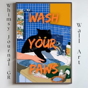 May include: A framed wall art print featuring a black cat washing its paws in a bathroom sink. The words "WASH YOUR PAWS" are in orange block letters. The background includes blue tile, an orange towel, and a floral patterned shower curtain.