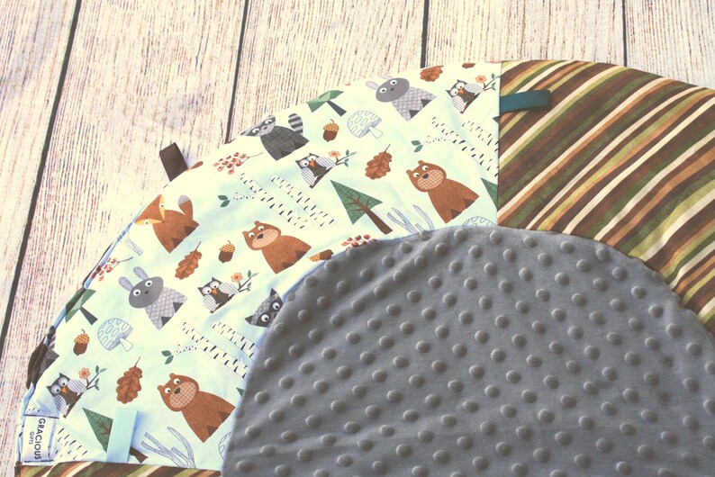 Puede incluir: Una alfombra de juego redonda, gris y blanca con estampado de animales del bosque. La alfombra tiene una superficie suave y texturizada, ideal para beb&eacute;s y ni&ntilde;os peque&ntilde;os.