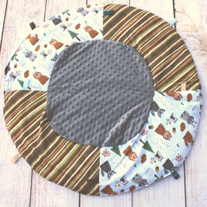 Puede incluir: Una alfombra de juego redonda, gris y marr&oacute;n con estampado de animales blanco y marr&oacute;n. La alfombra tiene un centro suave y texturizado y un borde exterior a rayas.