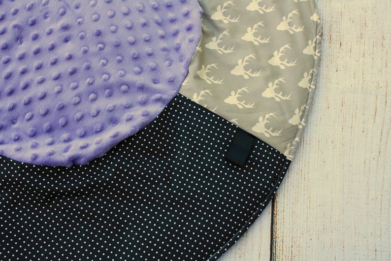 May include: A round, multi-colored play mat with a purple, black and white polka dot, and gray fabric with white deer silhouettes.