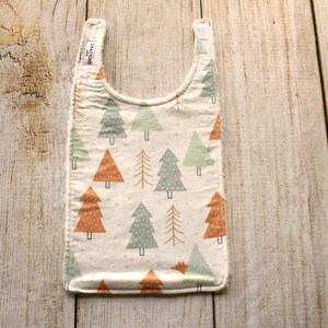 May include: A white bib with a pattern of green and orange trees. The bib has a small label that says "Gracious" on it.