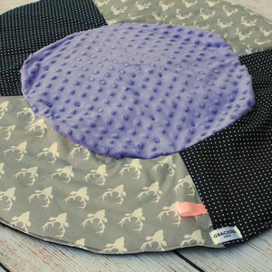 May include: A round, multi-colored baby play mat with a purple center, black and white polka dot fabric, and gray fabric with a white deer print. The mat has a pink ribbon and a black tag with the text "Gracious Gifts".