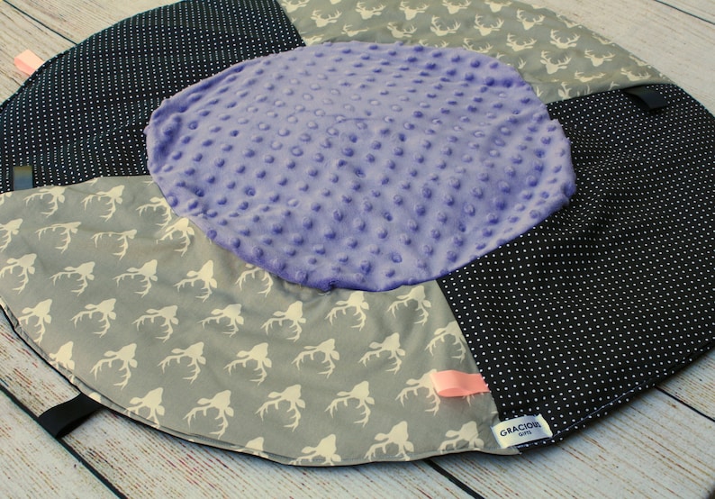 May include: A round, multi-colored baby play mat with a purple center, black and white polka dot fabric, and gray fabric with a white deer print. The mat has a pink ribbon and a black tag with the text "Gracious Gifts".