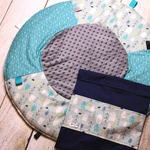 Puede incluir: Una alfombra de juego redonda multicolor con un círculo central gris y una bolsa de almacenamiento azul y blanca con el texto "Bracoos" impreso en ella.