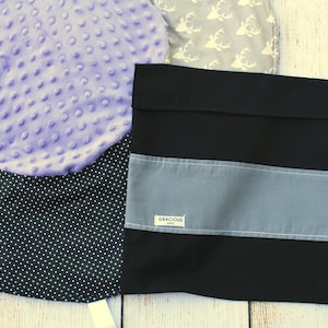 May include: A black fabric storage bag with a gray stripe and the text "Gracious Gifts" on a white label. The bag is lying on a white wooden surface.