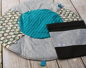 May include: A round, gray and white play mat with a turquoise center circle and a black and white skull pattern. The mat has a black storage pouch with the word "Gracious" printed on it.