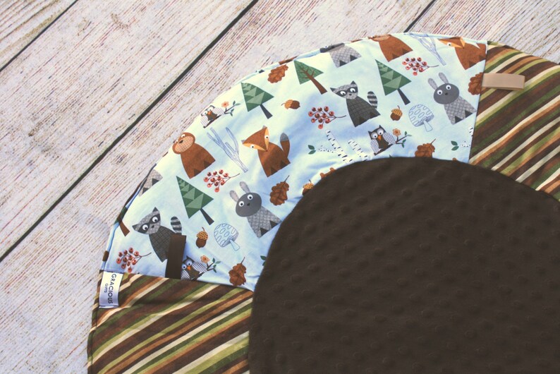 Puede incluir: Una alfombra de juego para beb&eacute;s de color marr&oacute;n y azul con un tema de animales del bosque. La alfombra tiene un centro suave y texturizado y un anillo exterior colorido con una variedad de animales, incluyendo un zorro, un mapache, un b&uacute;ho y un oso. El anillo exterior est&aacute; hecho de tela a rayas.